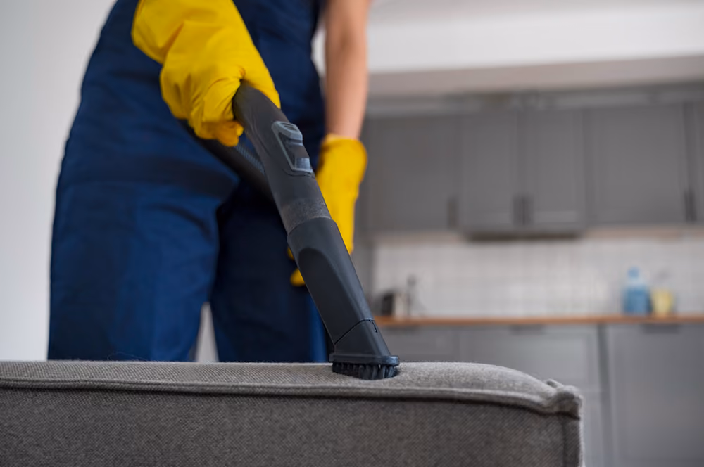 Grund- und Sonderreinigung: Reinigungskraft in Firmenkleidung reinigt Polstermöbel mit einem speziellen Gerät.