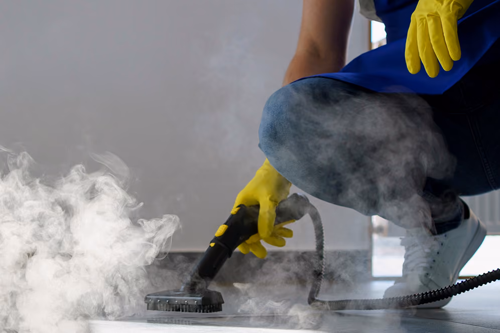 Bauendreinigung: Reinigungskraft in Arbeitskleidung reinigt den Boden mit einem speziellen Dampfreinigungsgerät.