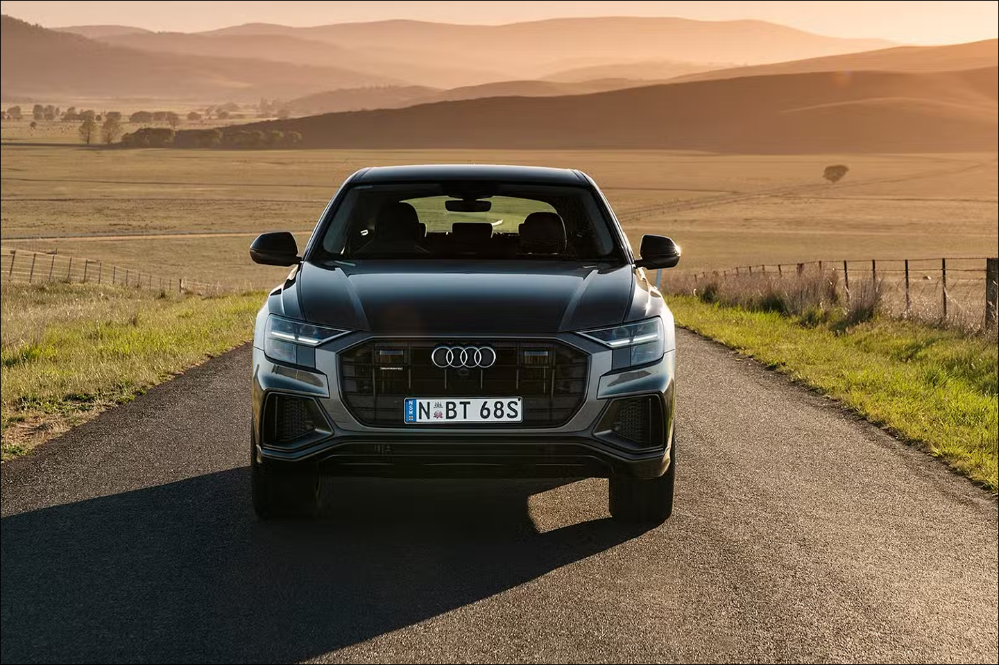 Фронтальний вид чорного автомобіля Audi на порожній дорозі поміж полями та горами.