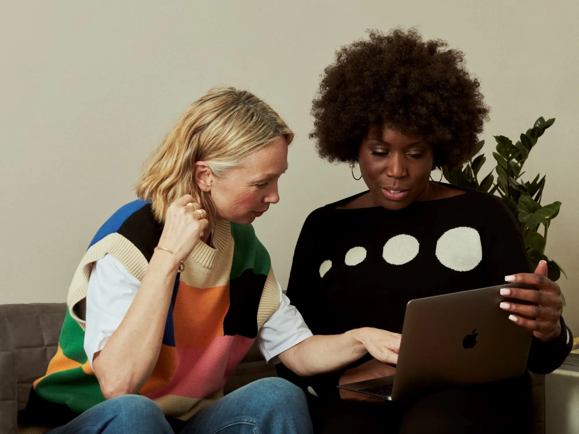 Zwei Frauen sitzen zusammen und schauen auf einen Laptop, eine zeigt auf den Bildschirm.