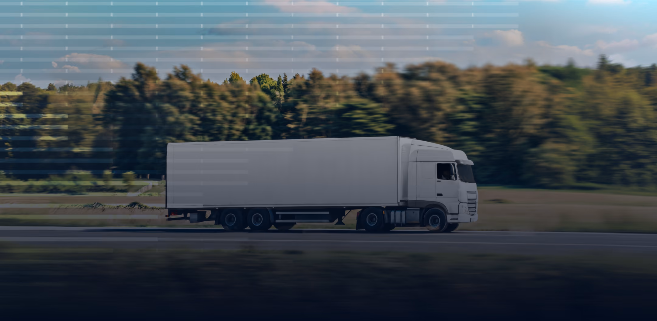 White semi-truck driving on a highway with green trees and a clear sky background.