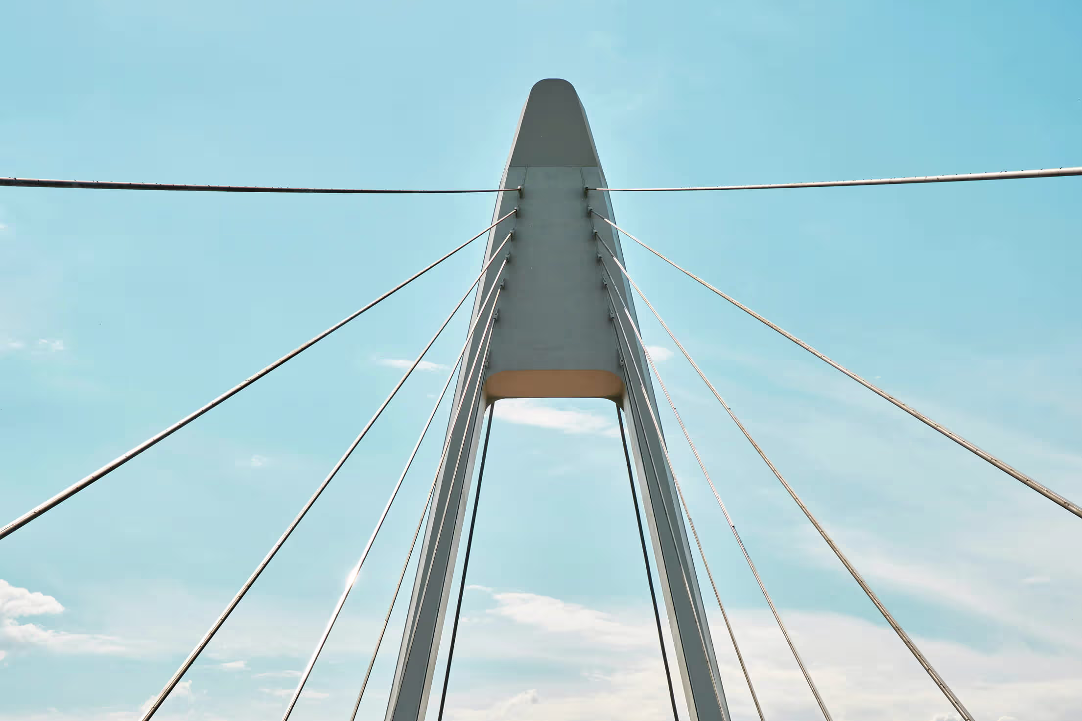 Close-up view looking up at a cable-stayed bridge's pylon and support cables against a clear blue sky.