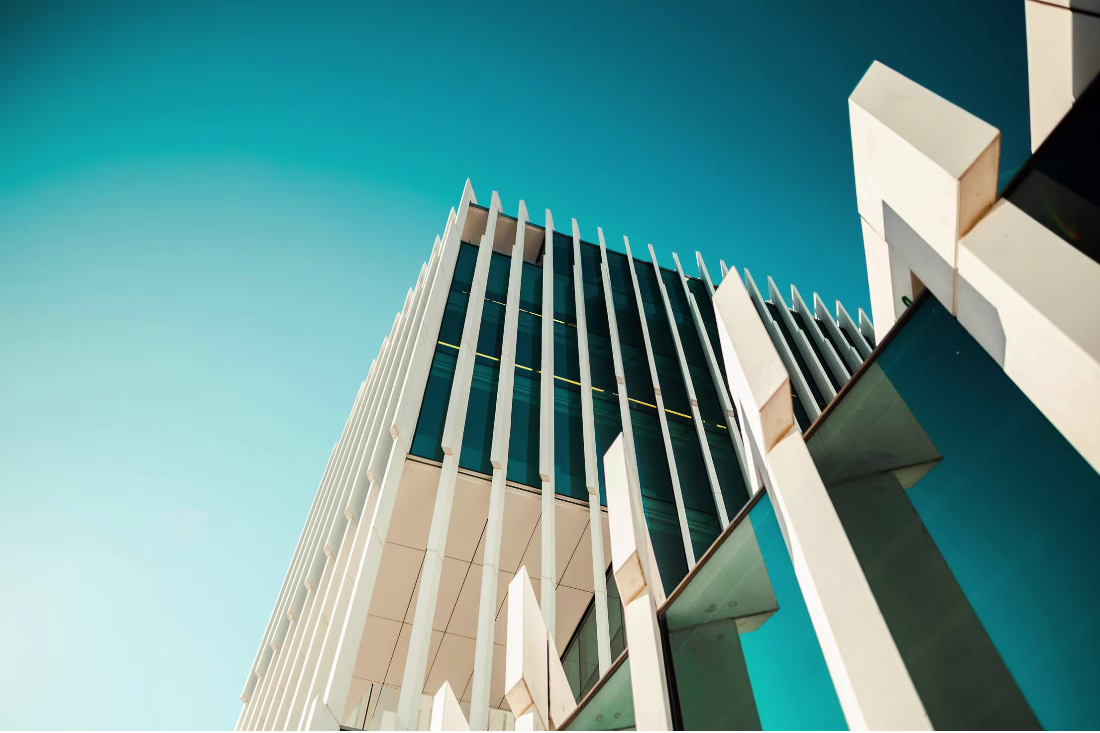 Symmetrical low-angle view of two glass and stone skyscrapers meeting at a point, with blue sky filling the left side.