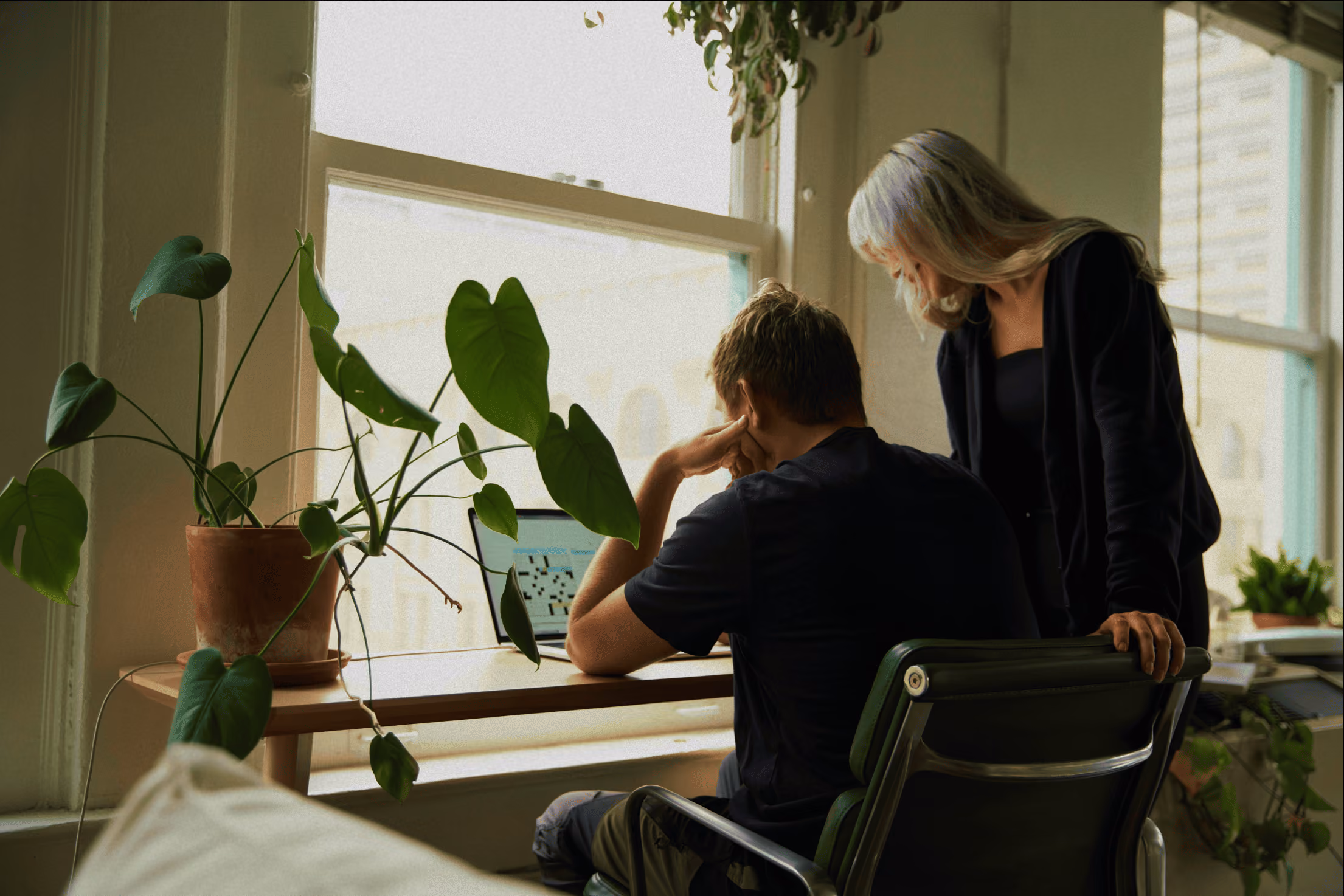 One person sitting down looking at a laptop and another looking at it over their shoulder
