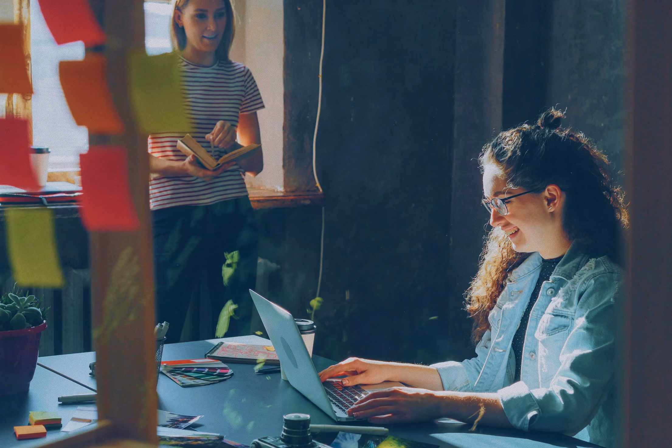Someone looking at a laptop with someone else next to them reading a book.