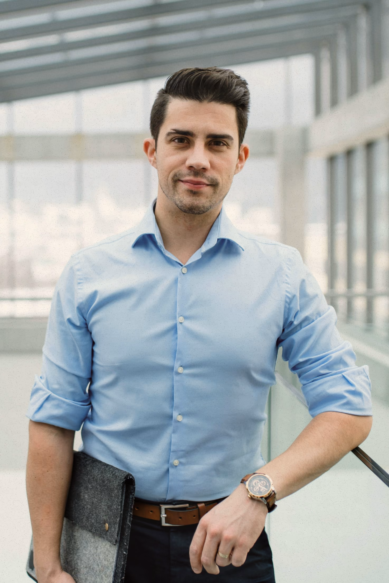 Man in blue shirt holding a gray felt folder in a modern glass building lobby.
