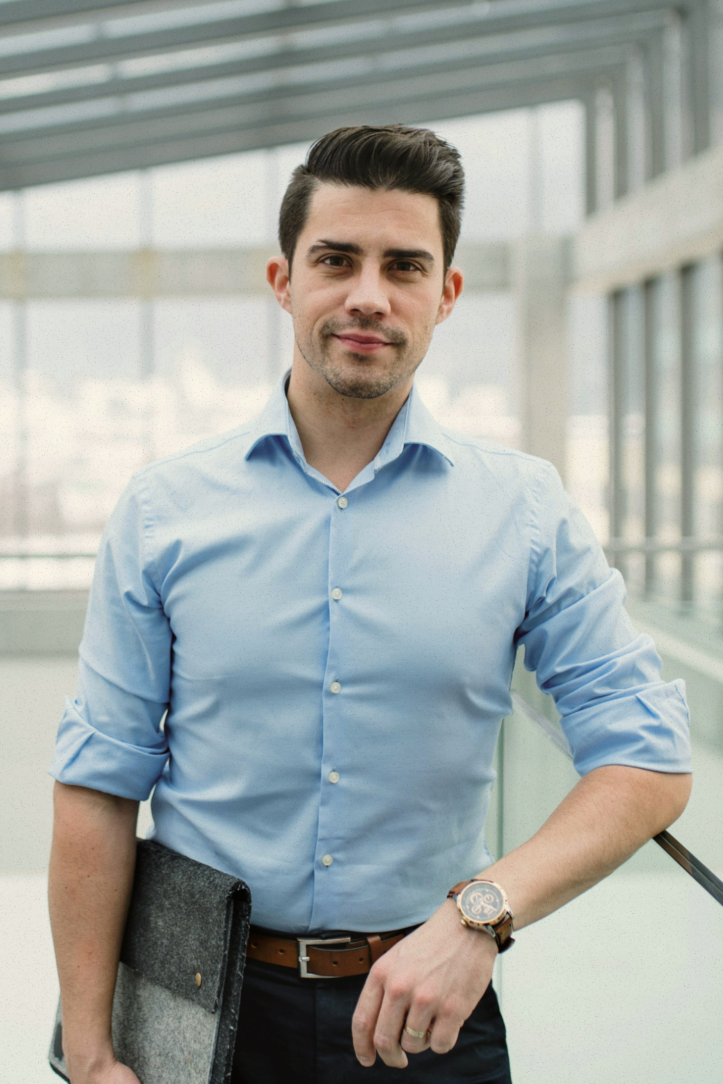 Man in blue shirt holding a gray felt folder in a modern glass building lobby.