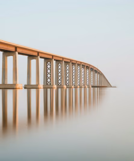 Long bridge extending across calm, misty water with clear reflections of the bridge's pillars and structure.