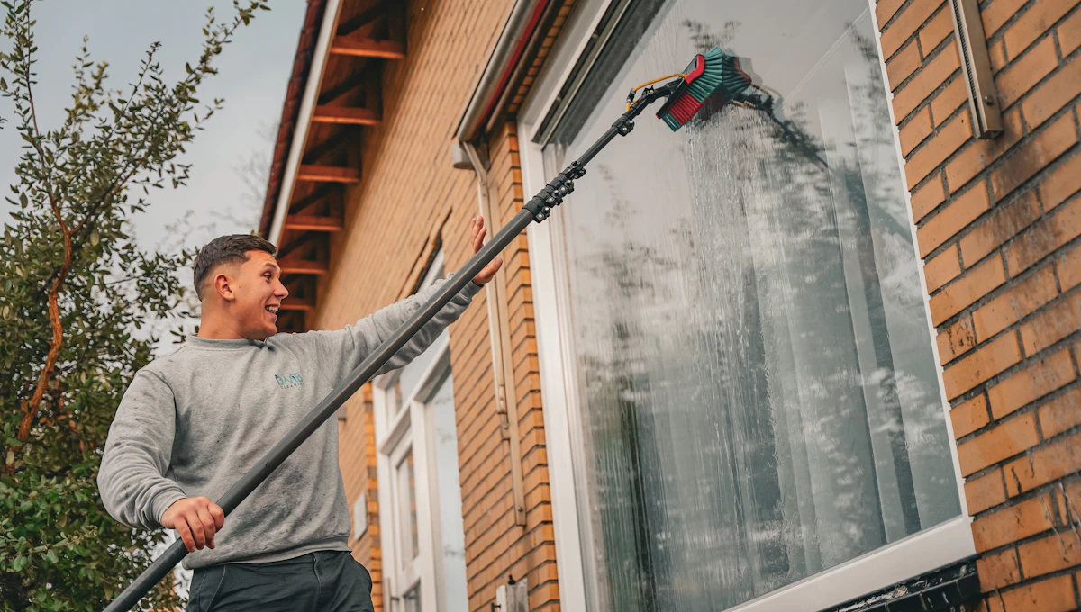 Nettoyage d'une grande fenêtre de maison avec une perche