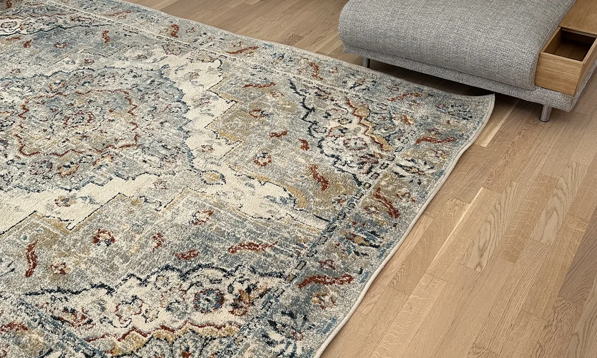 Tapis de salon à motifs bleus et beiges devant un canapé gris, chez un client