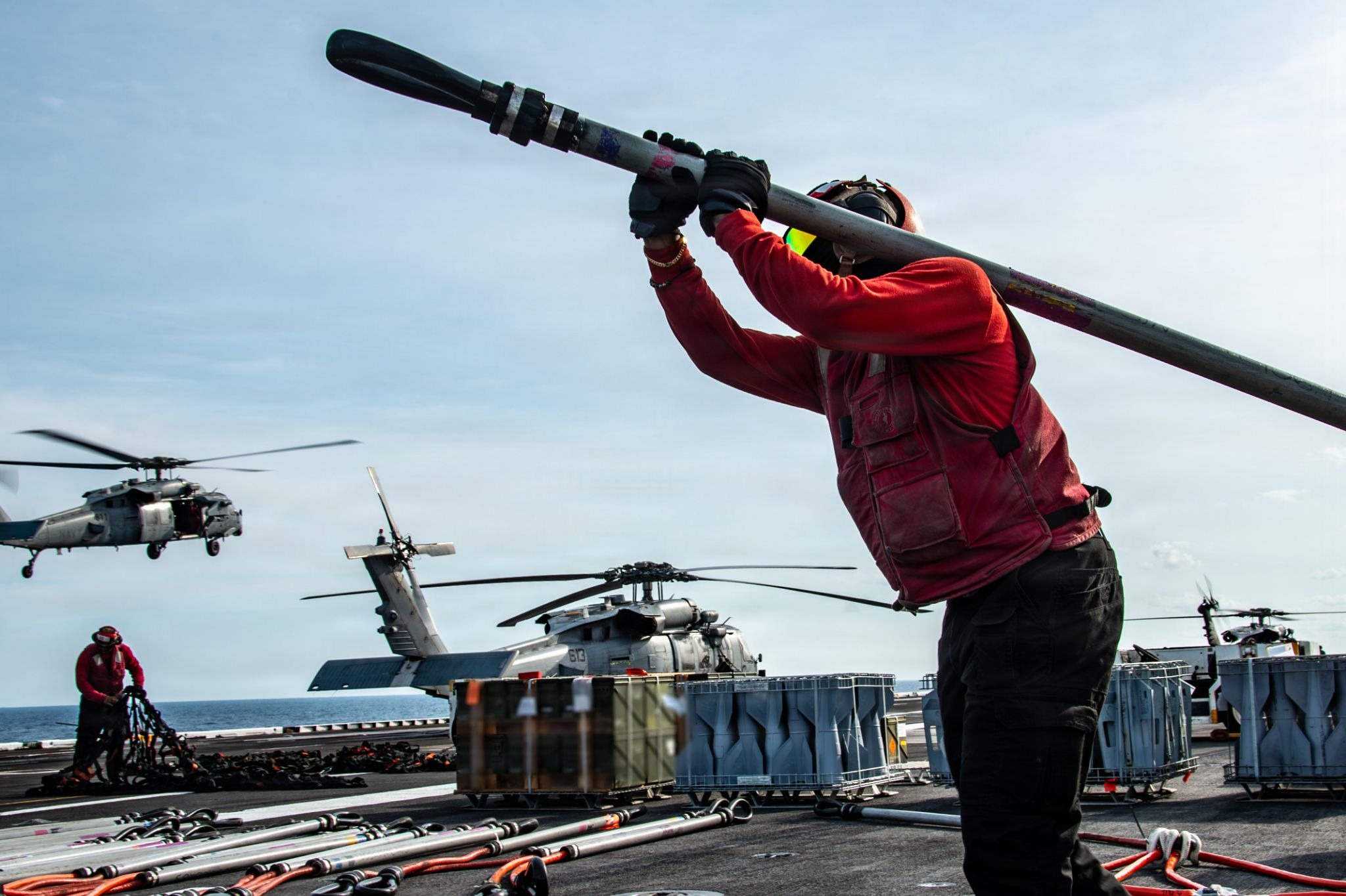 A Sailor moves an attaching cable during an ordnance offload on an aircraft carrier flight deck.