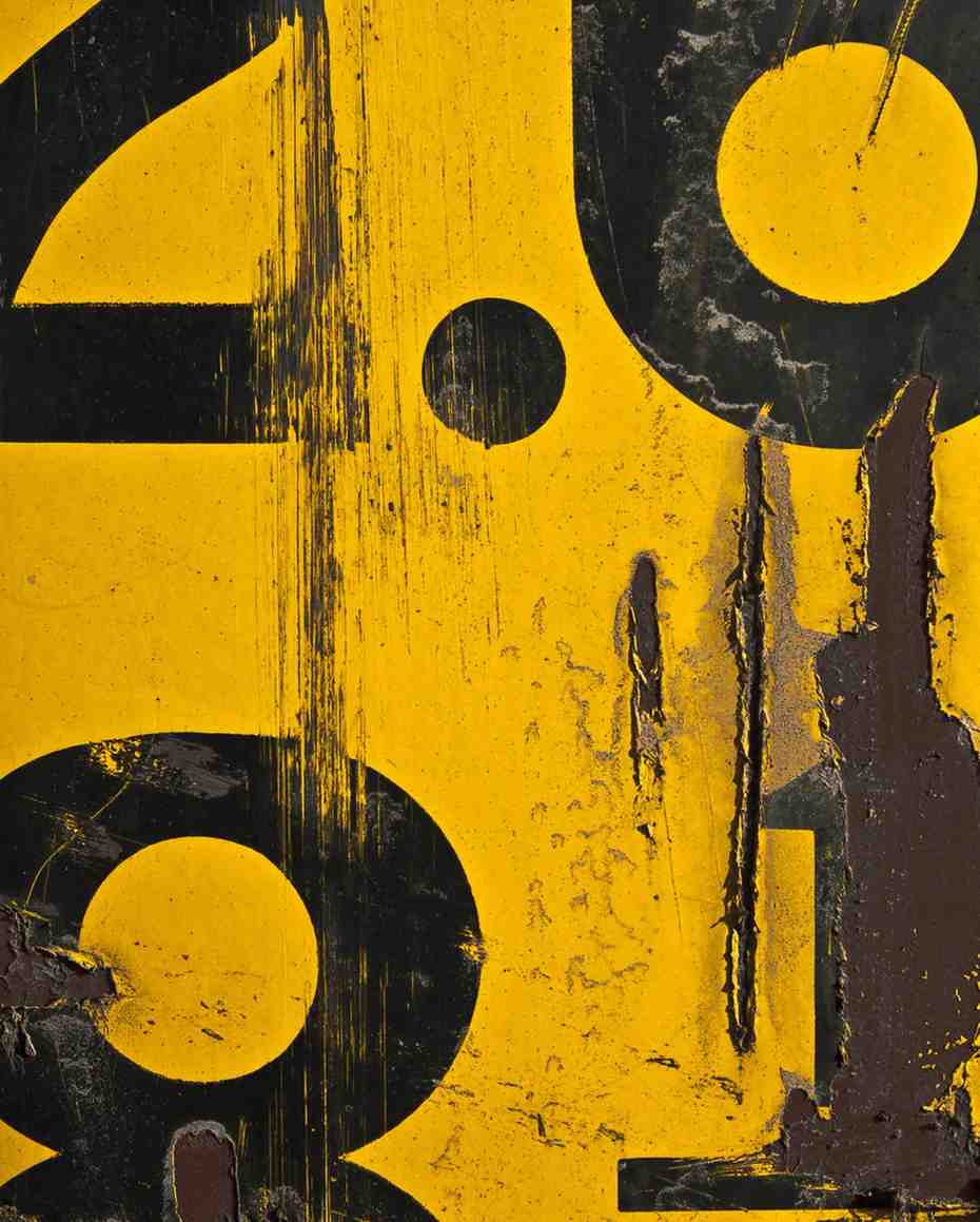 Close-up of worn, scratched yellow surface with large black abstract shapes and peeling paint.