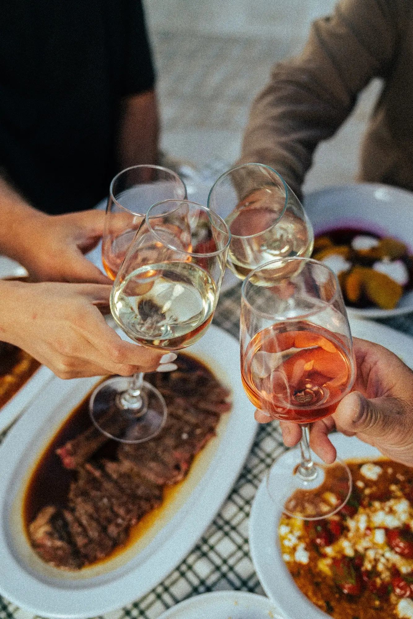 Four people toasting with white and rosé wine glasses over a table with dishes including steak and salad.