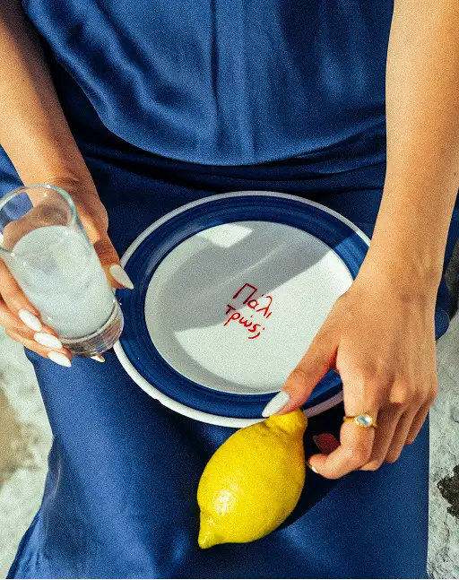 Person holding a circular mirror and a glass of water, with a lemon on their lap.