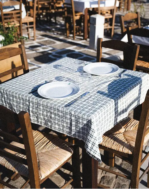 Outdoor dining table with a checkered tablecloth, two plates, glasses, and four wooden chairs.