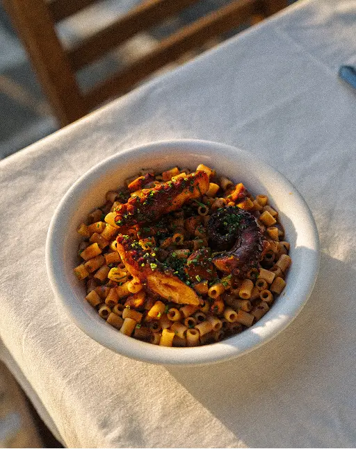 Bowl of pasta with tomato sauce and herbs on a table covered with a white cloth.