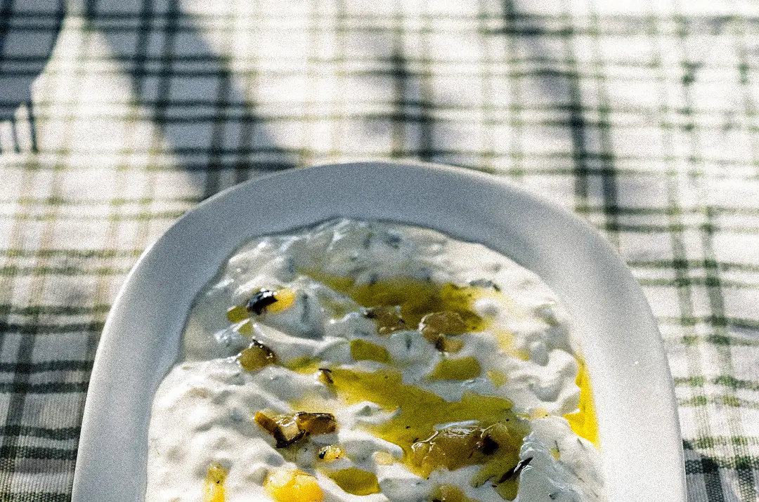 White dish with yogurt or cream sauce drizzled with olive oil and herbs on a plaid cloth.
