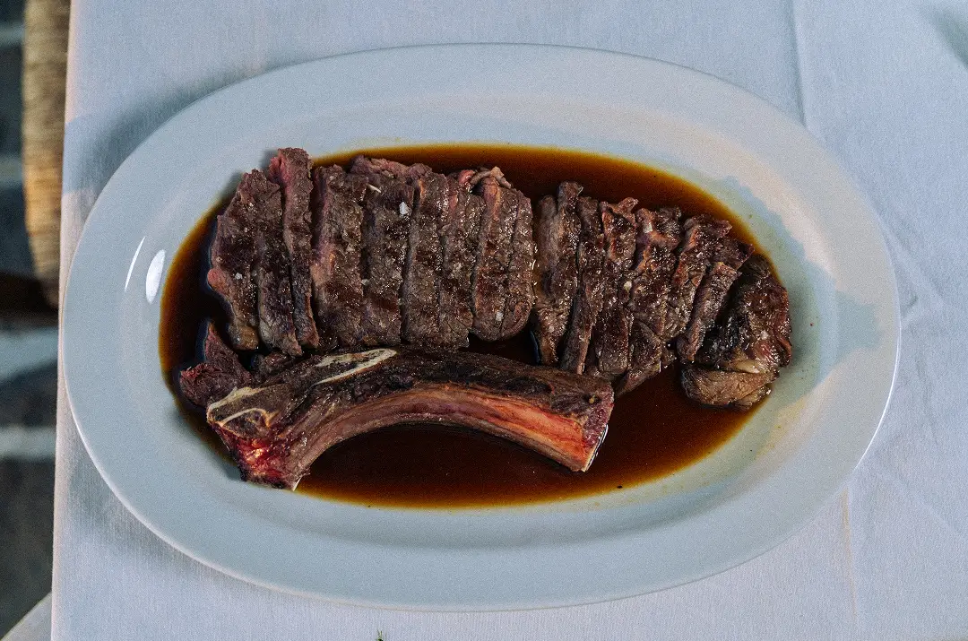 Sliced grilled steak with bone on white plate served with brown sauce on white cloth.
