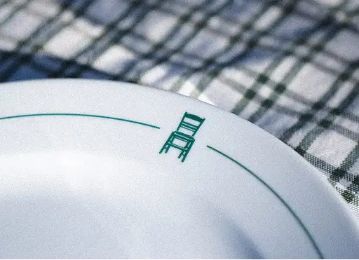 White plate with a green chair icon and a green line near the rim on a checkered tablecloth.
