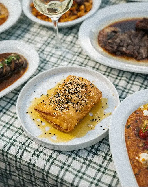 Plate with sesame-topped fried pastry drizzled with honey on a checkered tablecloth.