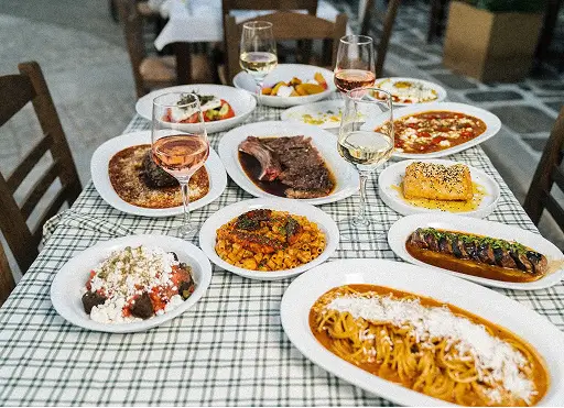 Table with various Italian dishes including pasta, steak, polenta, salad, and glasses of wine.