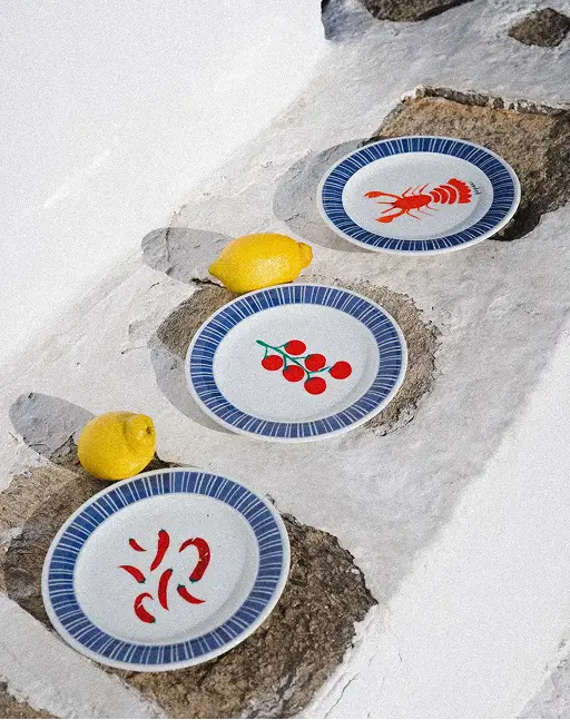 Three plates with blue rims on stone base, decorated with lobster, cherries, and red chili peppers; two lemons.