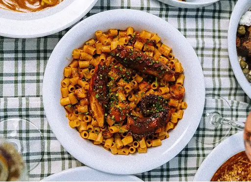 Plate of pasta with sauce and grilled octopus garnished with herbs on a checkered tablecloth.