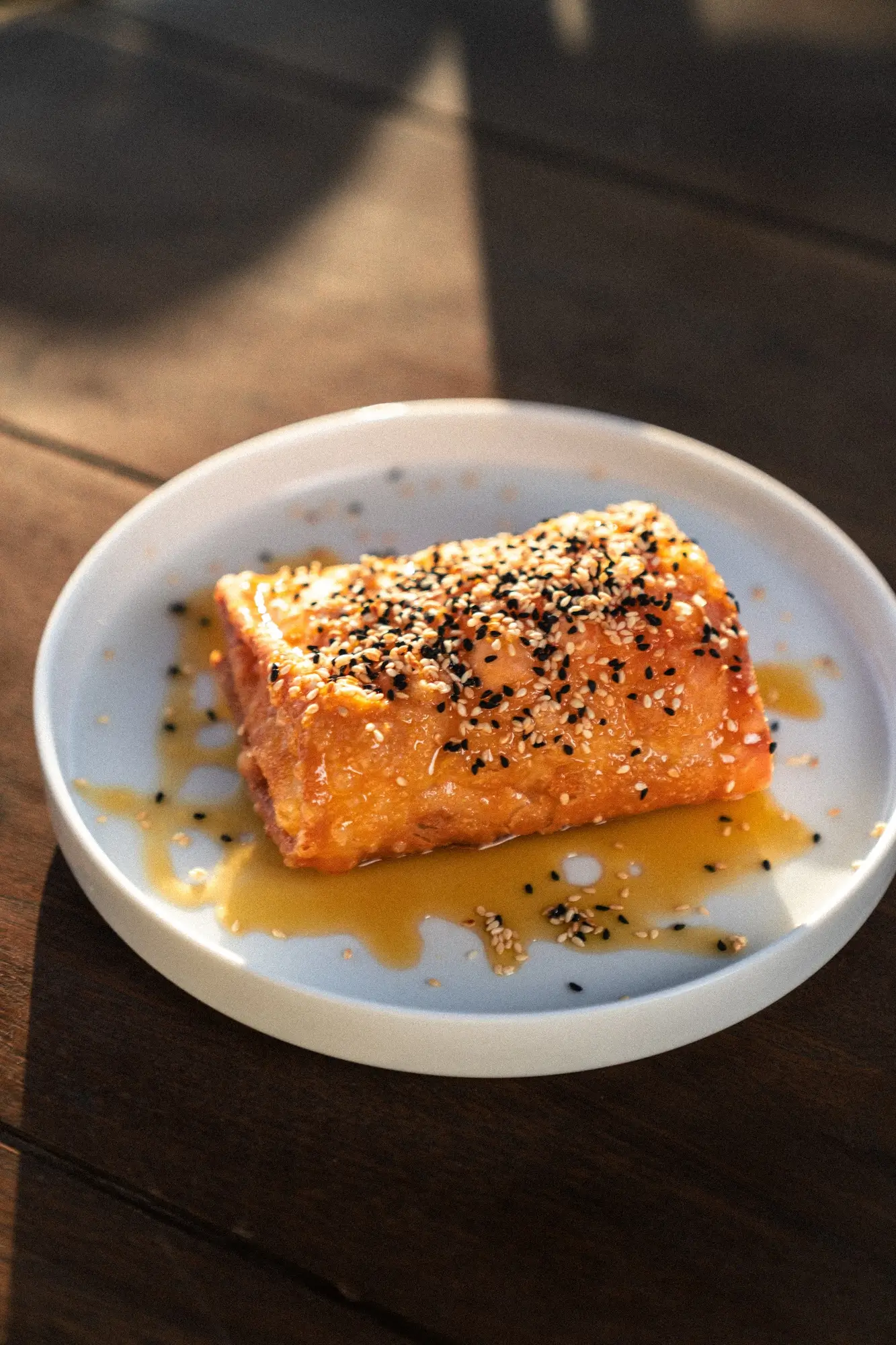 Glazed salmon fillet sprinkled with black and white sesame seeds on a white plate.