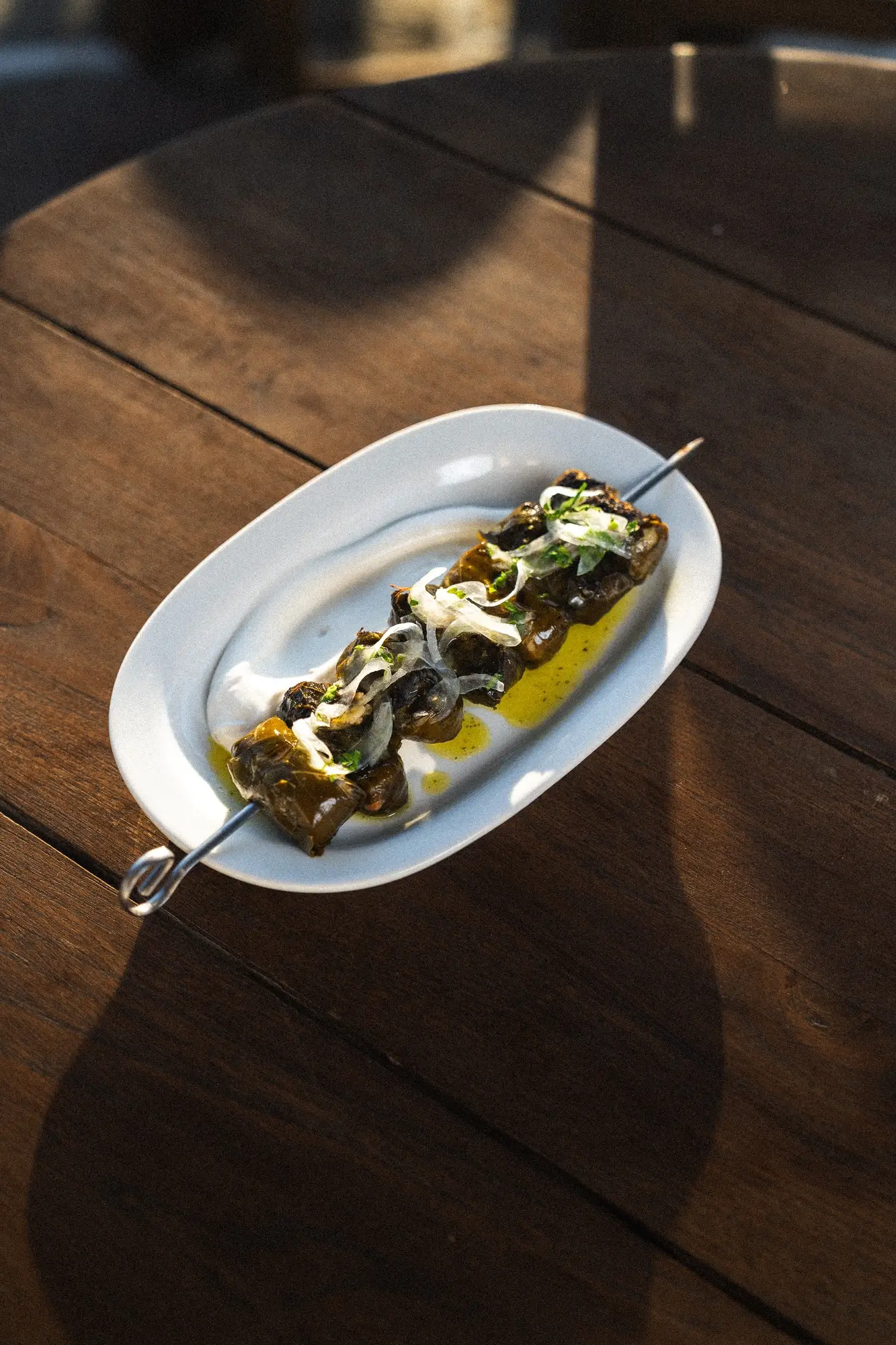 Skewer of grilled vegetables with onions and herbs served on a white plate with olive oil drizzle.