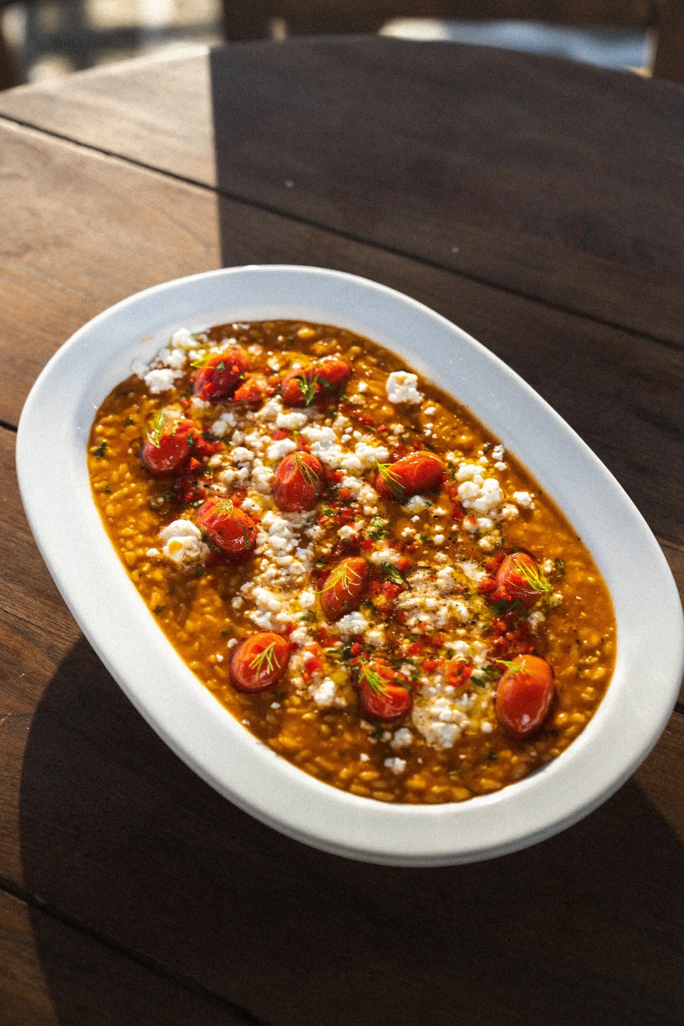 Plate of cooked lentils topped with cherry tomatoes, crumbled cheese, and herbs on a wooden table.