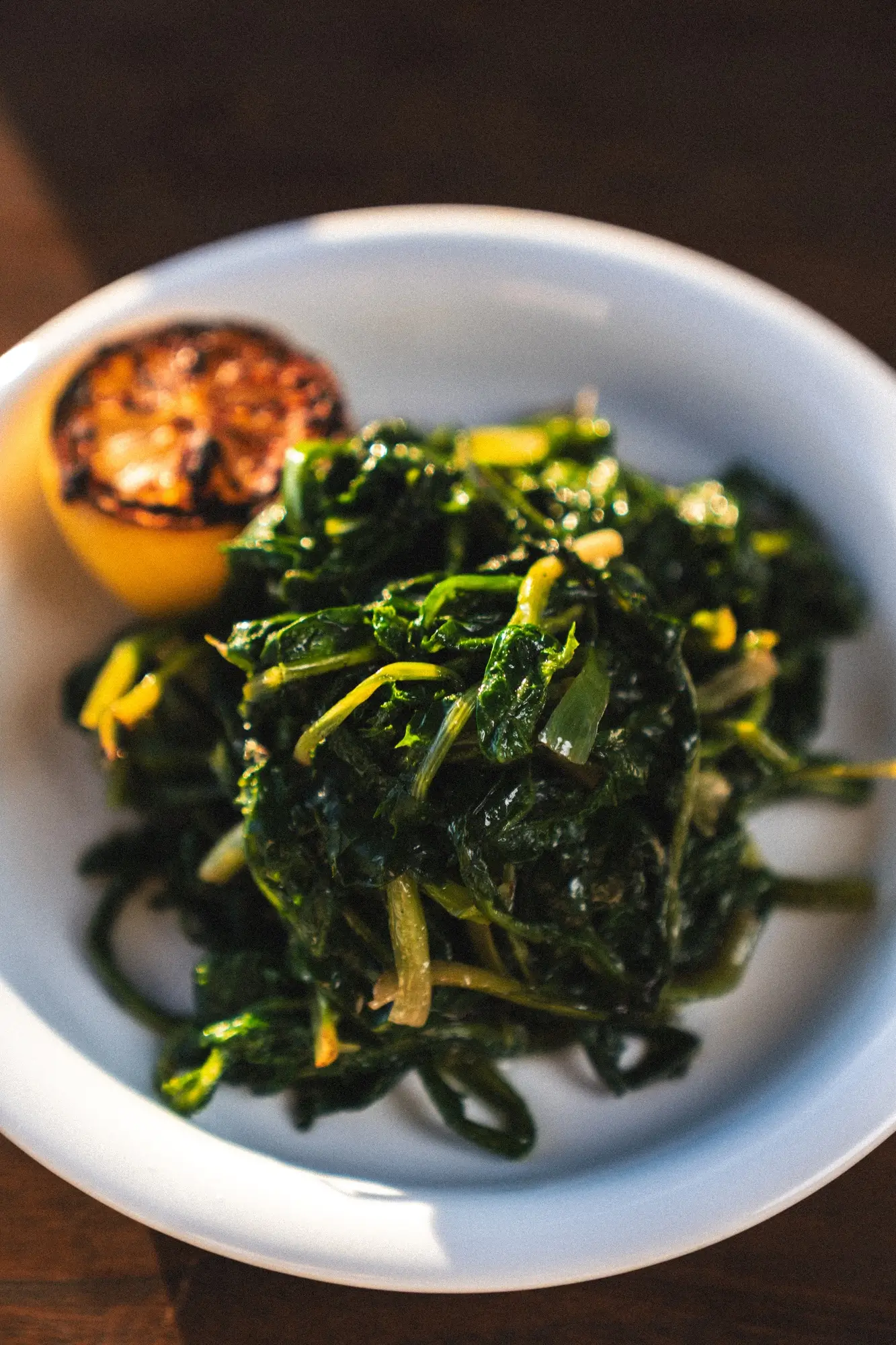 Cooked sautéed greens with a charred lemon half on a white plate.