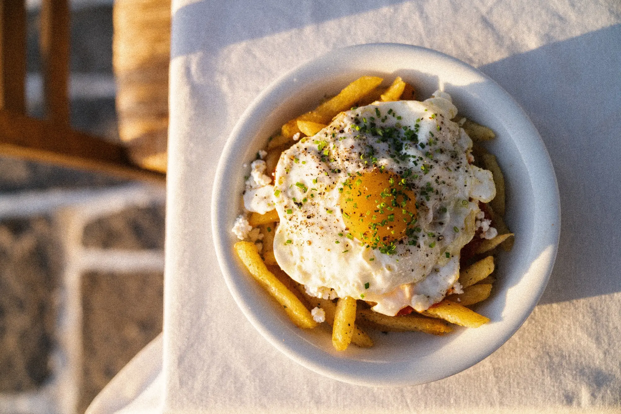 Fried egg with herbs on top of fries and cheese in a white bowl on a tablecloth.