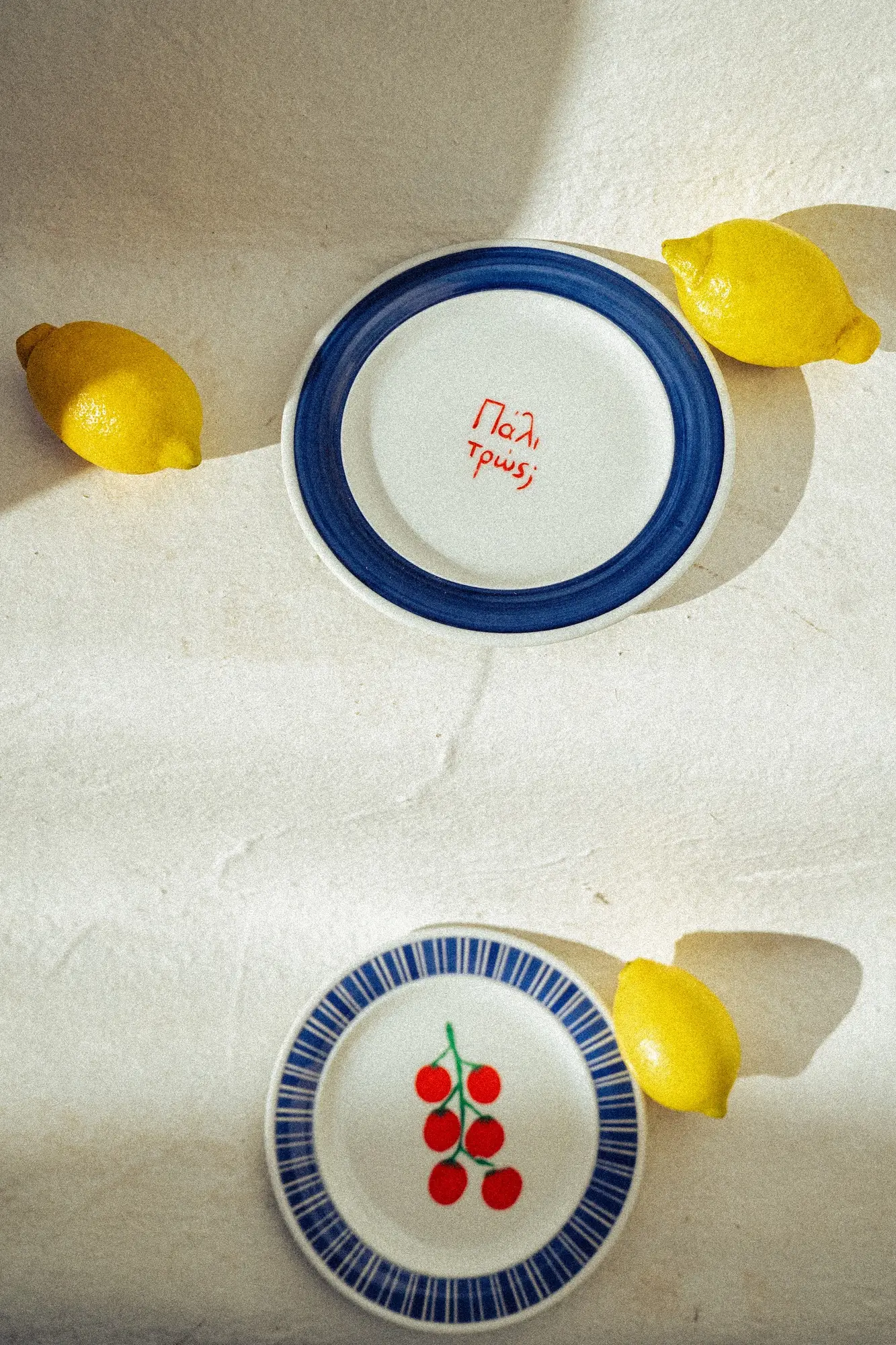 Two ceramic plates with blue borders on white surface with three lemons around them.