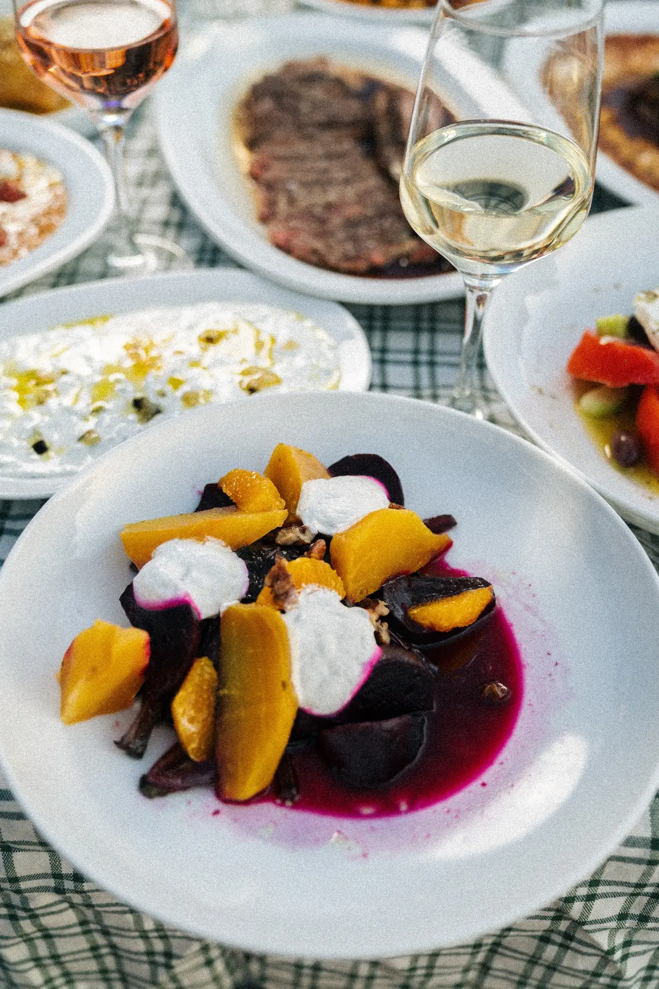 Plated salad with yellow and purple beets topped with white cream and walnuts, surrounded by wine and dishes.
