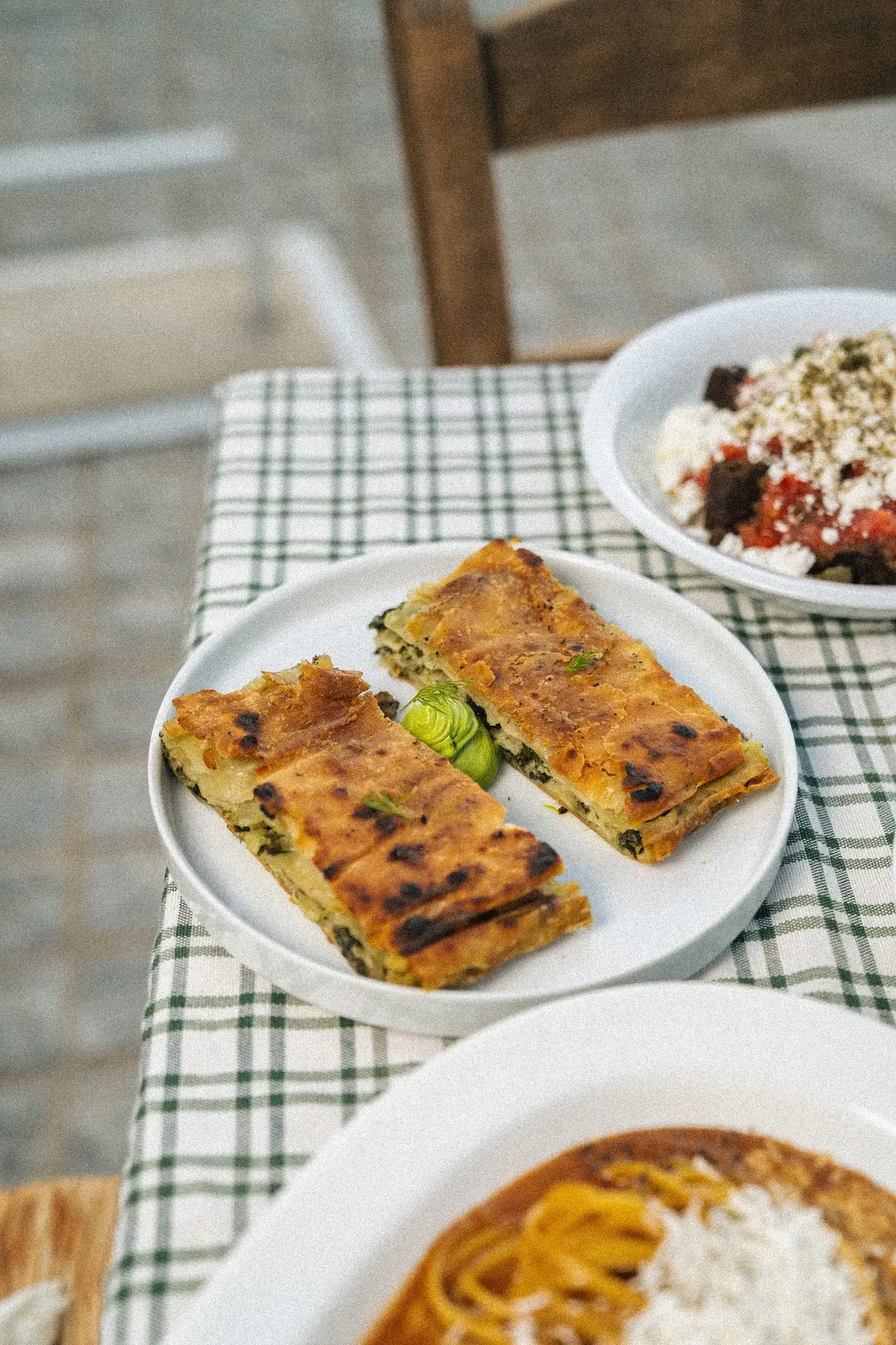 Two slices of golden-brown spinach pie on a white plate with dishes in the background.