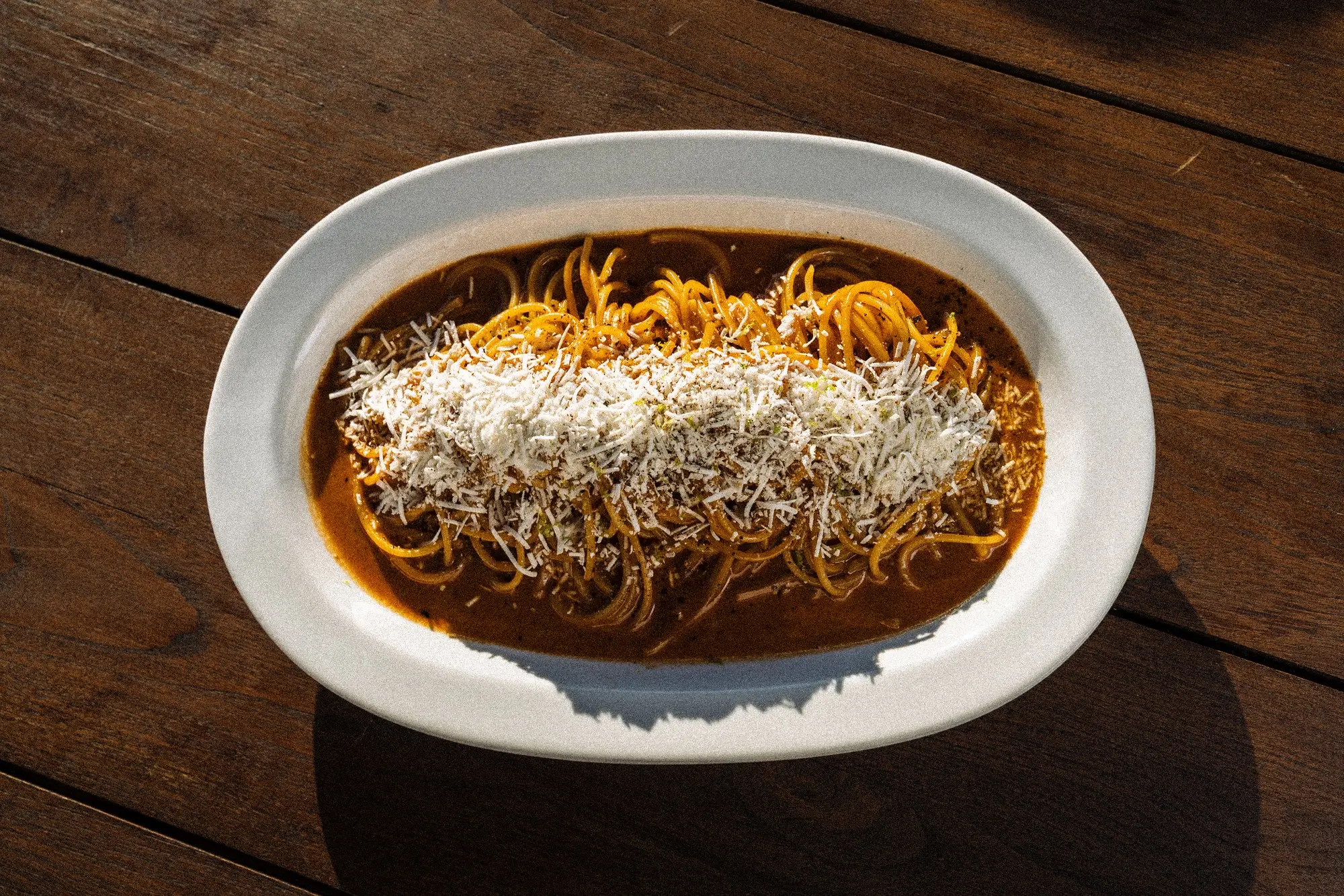 Plate of spaghetti topped with grated cheese and meat sauce on a wooden table.