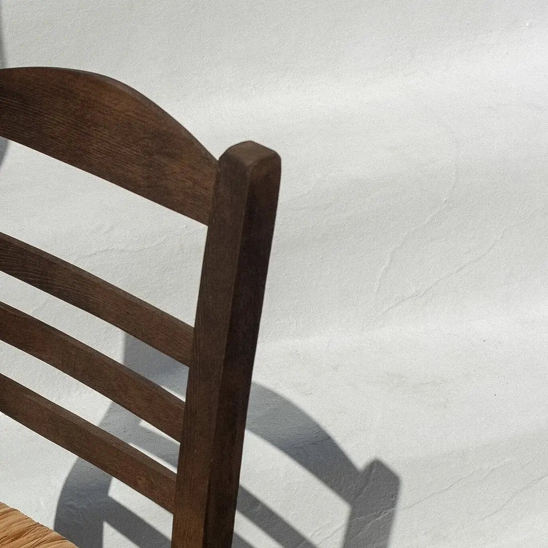 Close-up of a wooden chair back casting a shadow on a textured white wall.