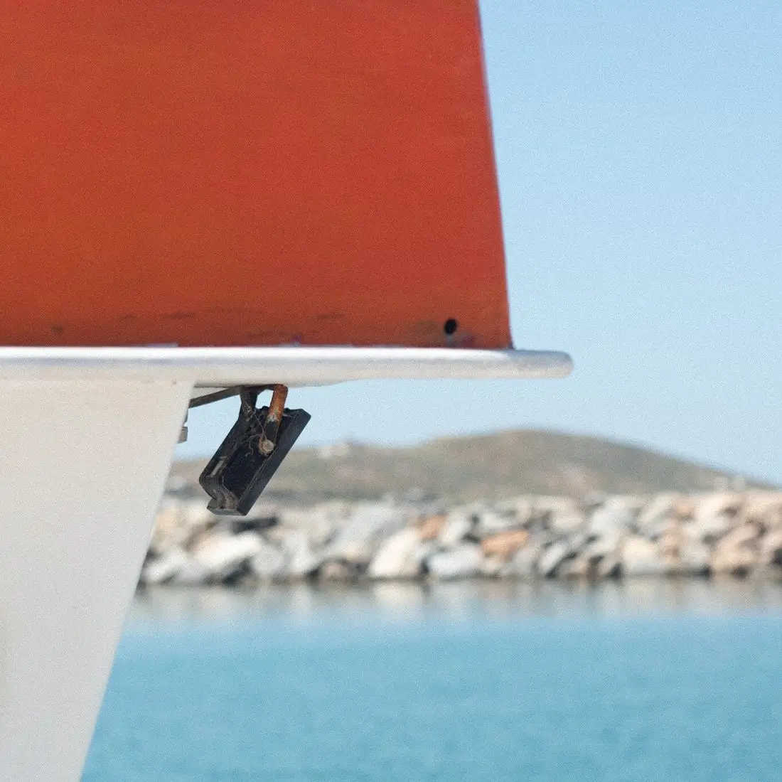 Close-up of a boat's red and white hull with water and rocky shore in the background.