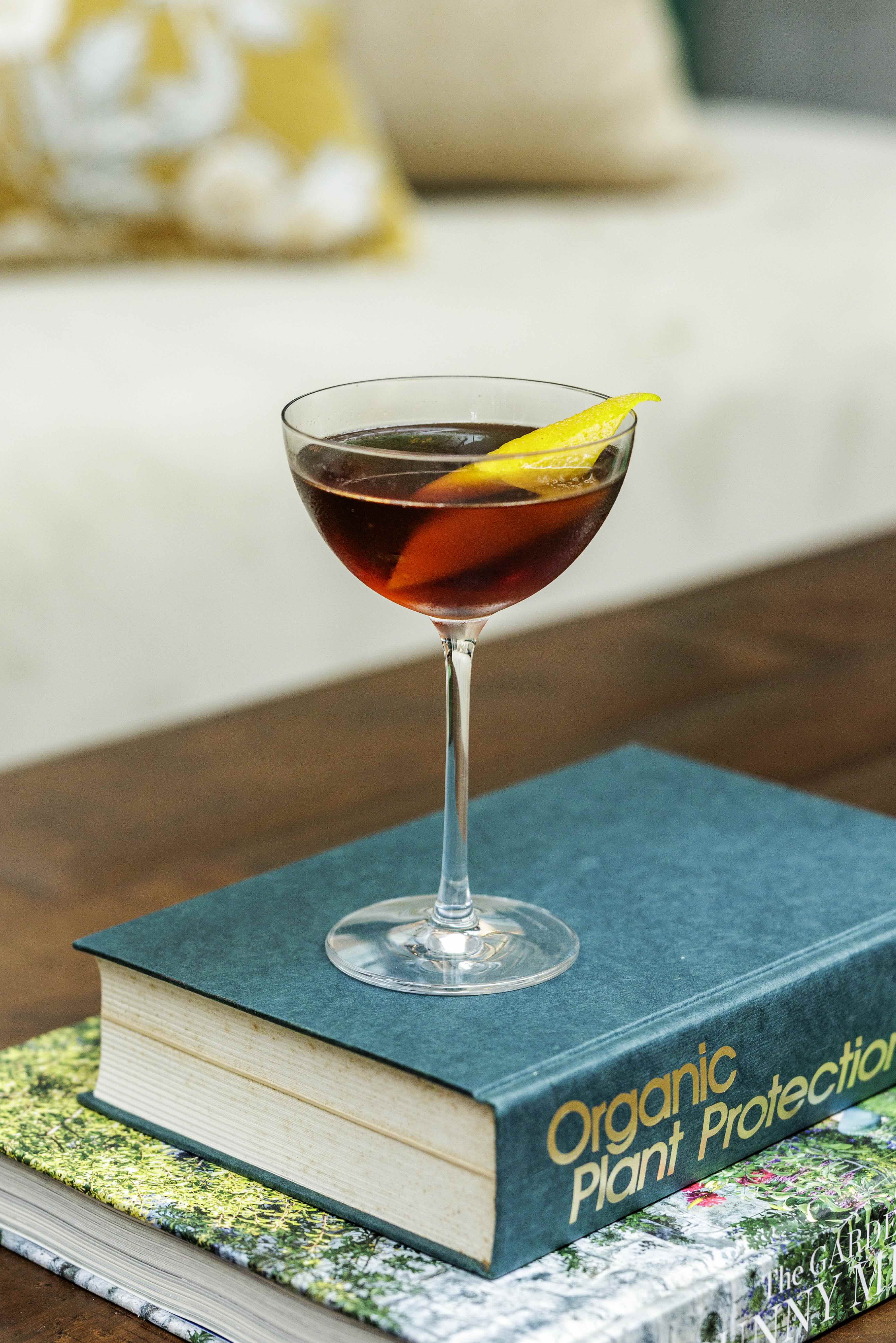 Whiskey cocktail with large ice cube and cherry garnish on a marble surface with black background.