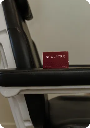 A small maroon box with 'Sculptra' on a black armrest of a medical chair.