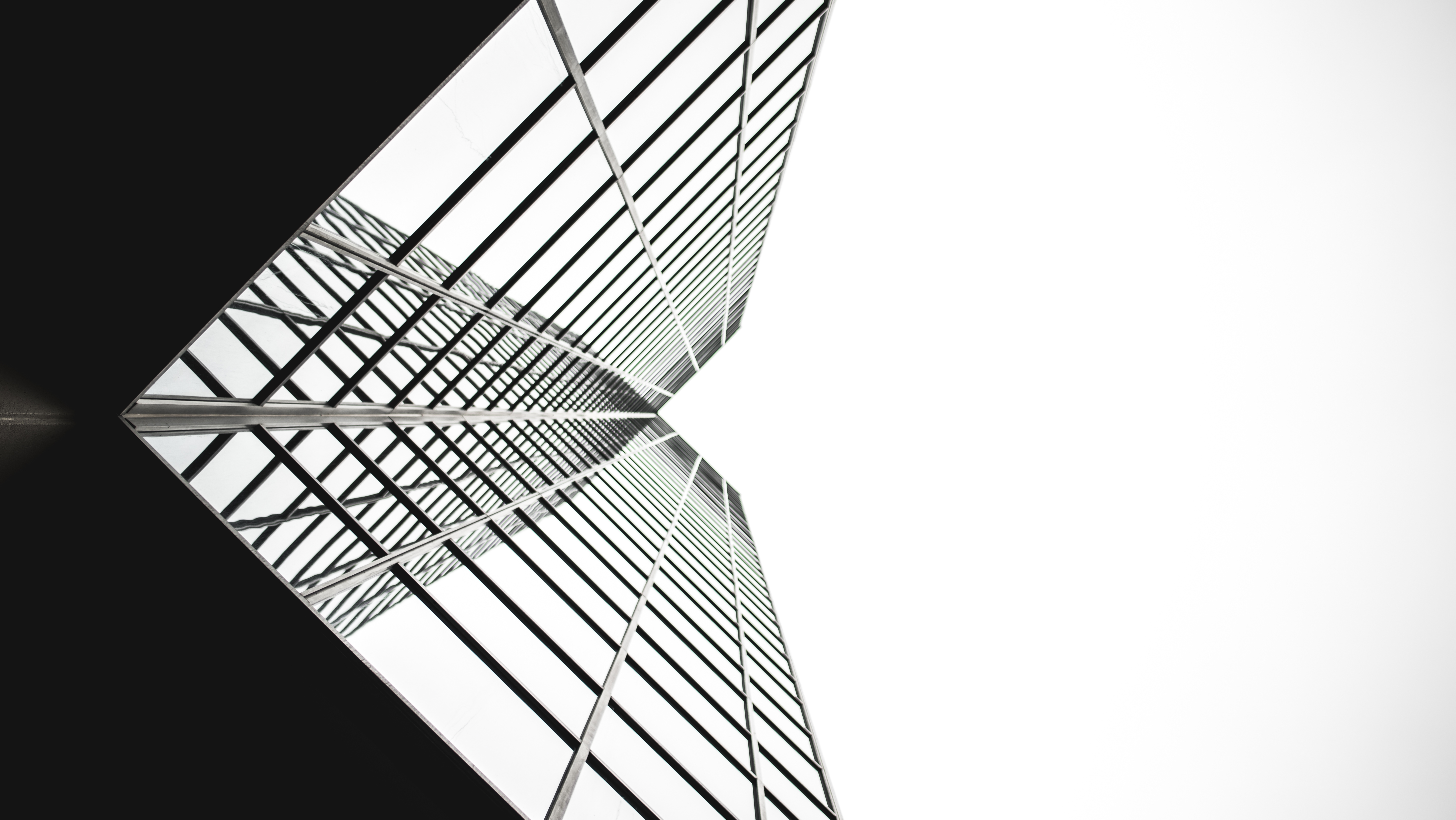 Upward view of a glass skyscraper reflecting its symmetrical facade with black window frames.