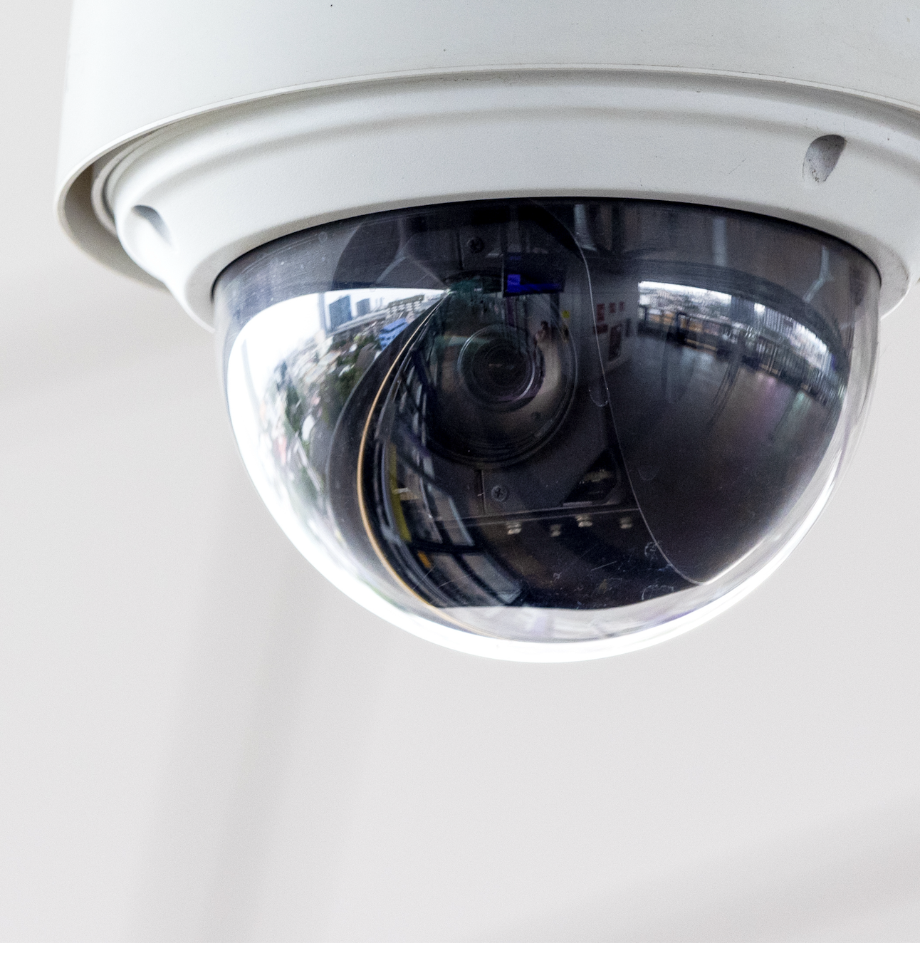 Close-up of a dome security camera mounted on a white ceiling indoors.