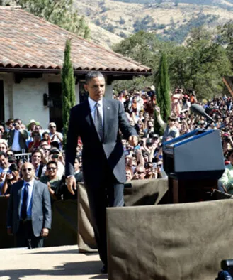 Historic photo of a speaker addressing a large crowd outside a tile-roofed building at La Paz