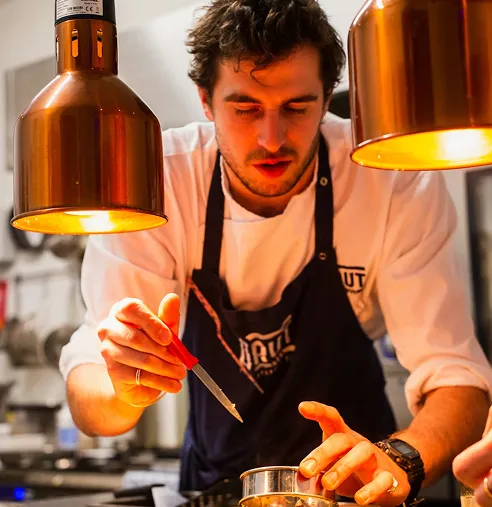 Executive Chef Jonathan Timbol plating a dish under copper heat lamps in the Villa La Paz kitchen