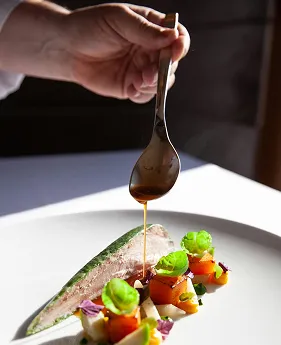Chef's hand spooning sauce over an artfully plated dish