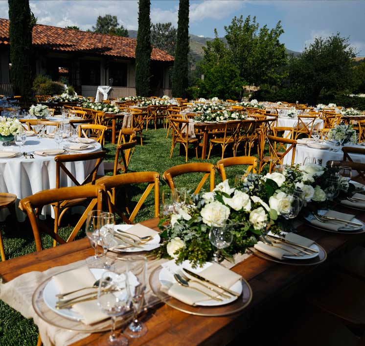 Outdoor wedding reception on the Villa La Paz lawn with farmhouse tables, crossback chairs, and white roses