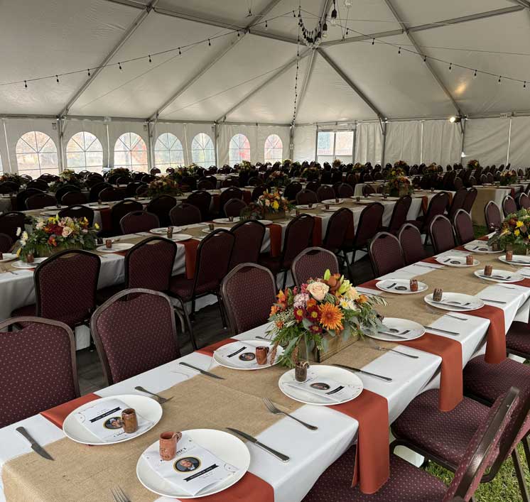 Long banquet tables with burlap runners, copper mugs, and autumn bouquets inside an event tent