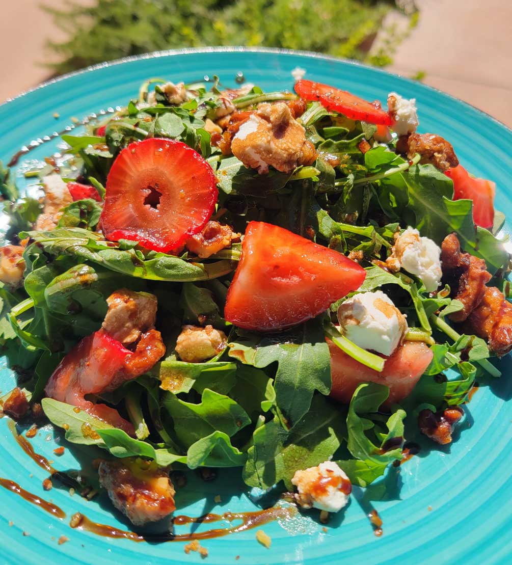 Strawberry and arugula salad with goat cheese and candied walnuts on a turquoise plate
