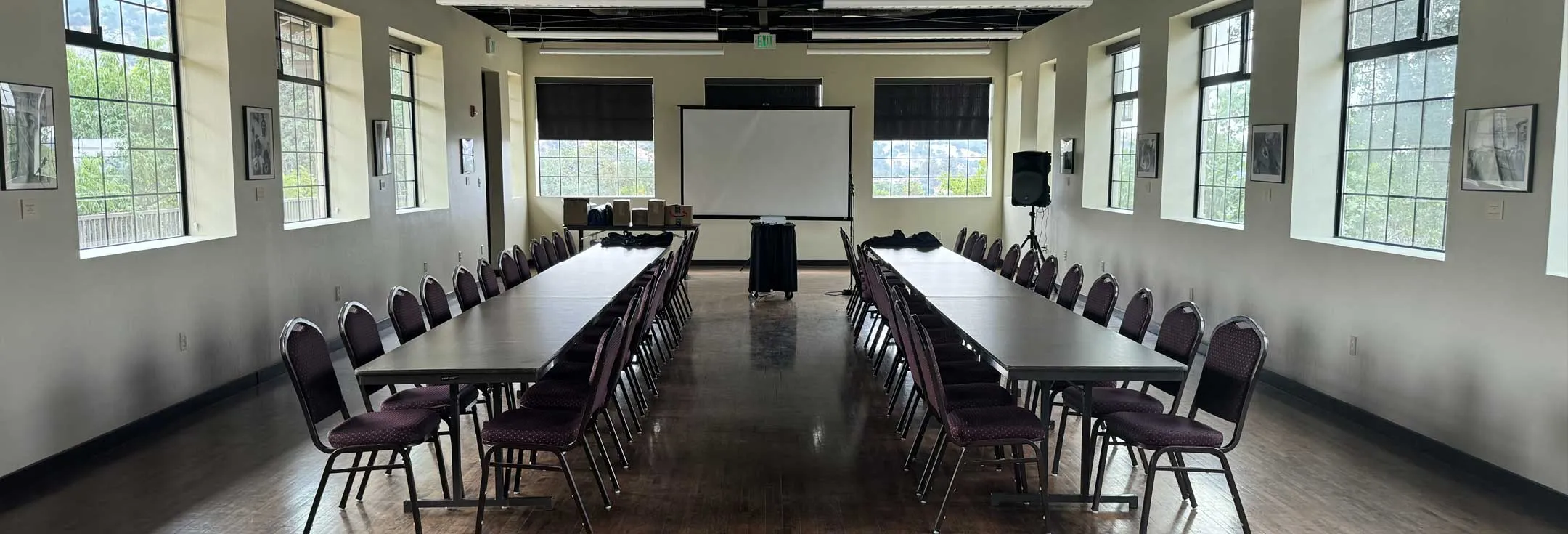 Boardroom-style meeting setup with long tables and chairs facing a projection screen