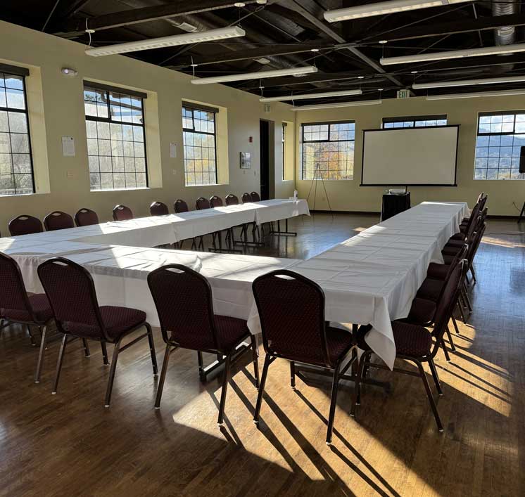 Sunlit meeting room with U-shaped conference tables and a projection screen